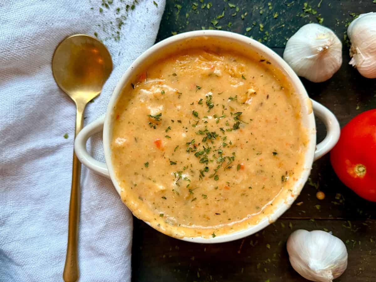 A bowl of roasted garlic soup with a spoon and veggies on the side.